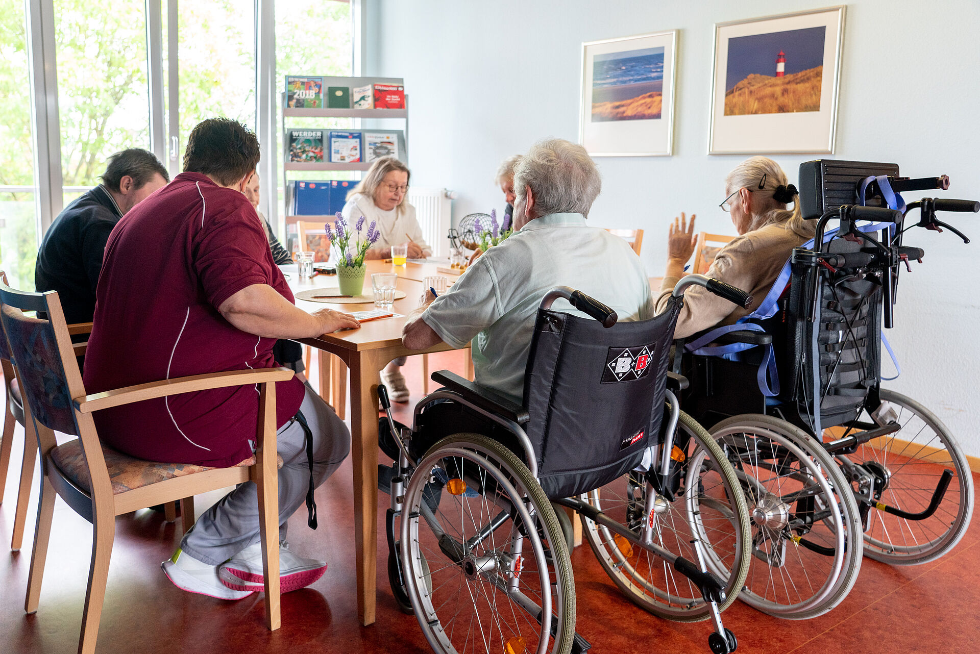 Eine Gruppe, darunter zwei Rollstuhlfahrer sitzt um einen Tisch.
