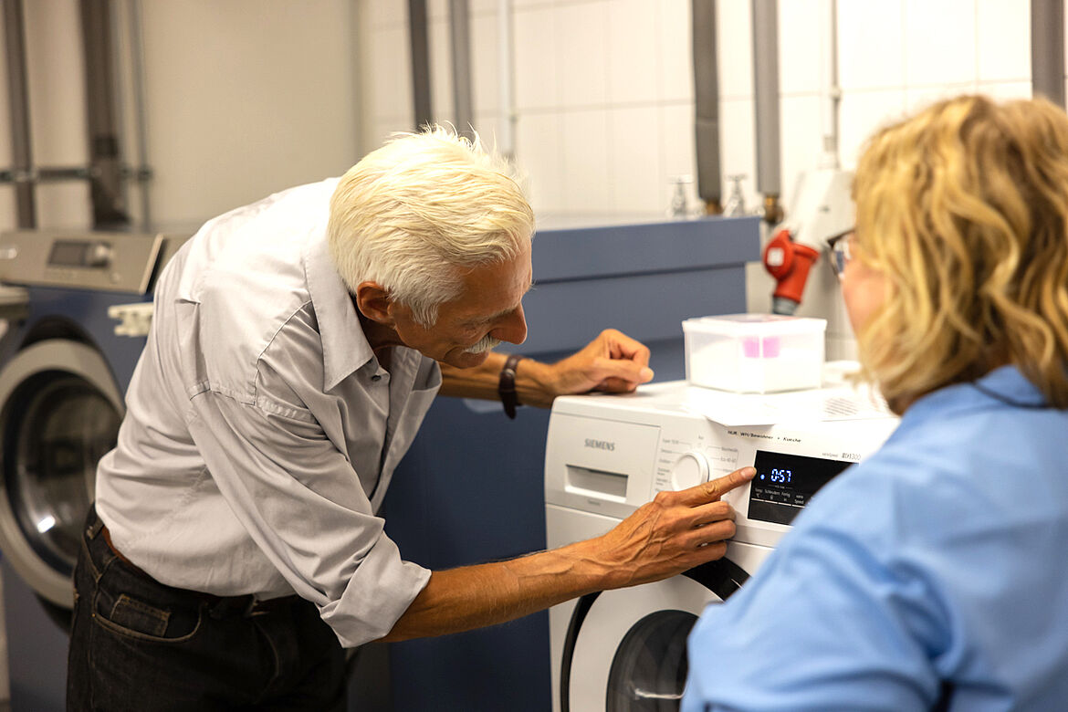 Auf der Waschmaschine stellt ein Bewohner des Besonderen Wohnform, die richtige Temperatur ein
