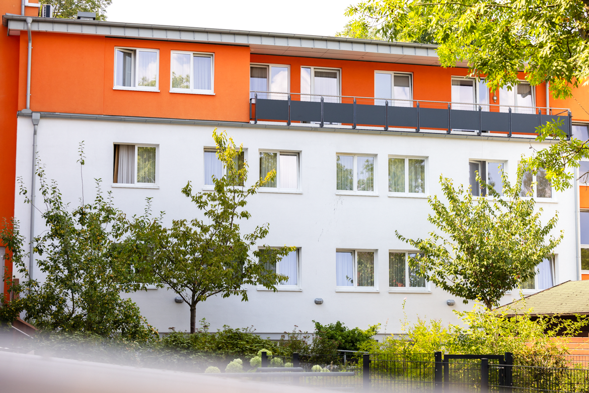 Bäume und Sträucher stehen vor der Fassade des Reha Hauses. 