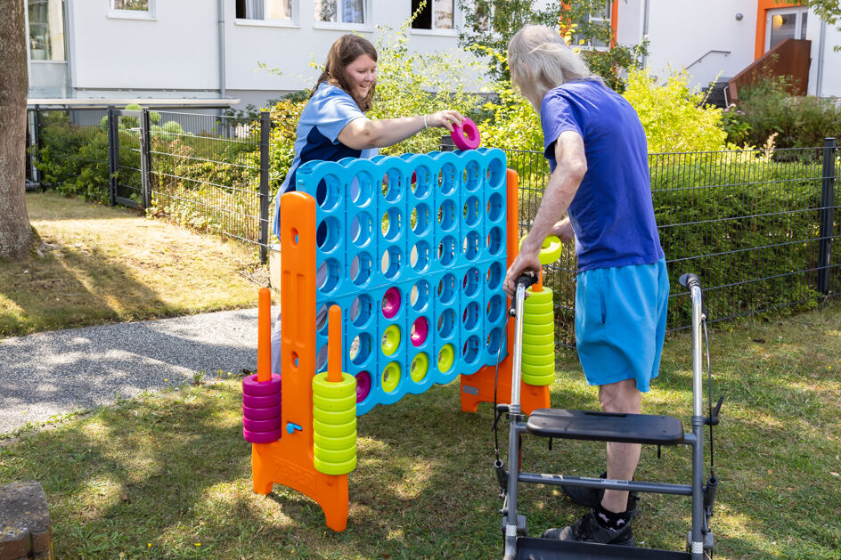 Ein Bewohner spielt mit einer Mitarbeiterin, im Garten, an einem großen 4-Gewinnt Spiel.