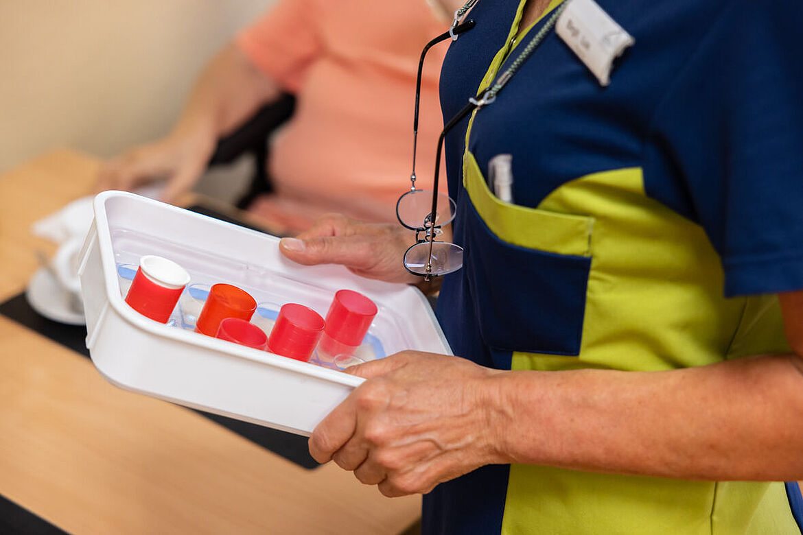 Eine Mitarbeiterin hält ein Tablett in den Händen, auf dem sich die Tablettenboxen der Bewohnenden befinden.