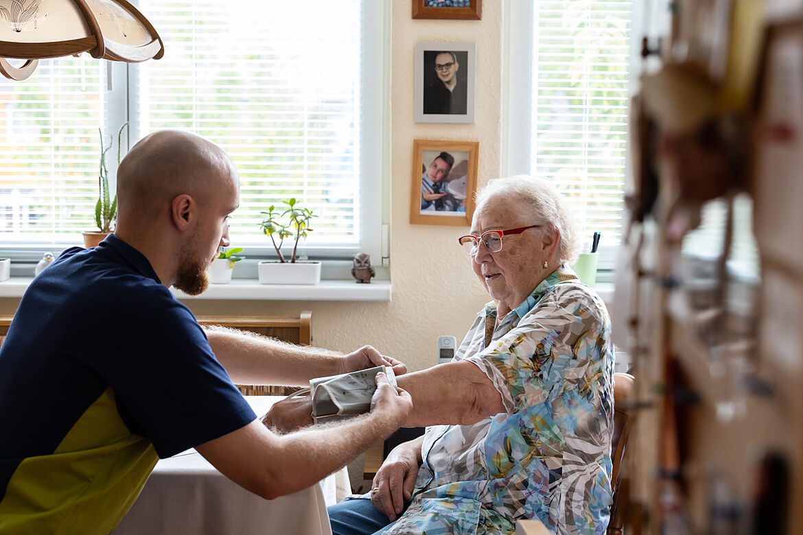 Ein Pfleger befestigt ein Blutdruckmessgerät an dem Arm einer älteren Dame (Bewohnerin)