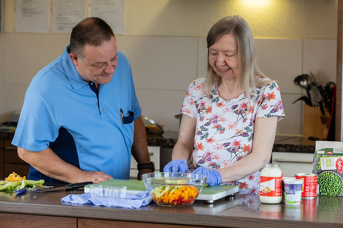 Ein Pfleger und eine Bewohnerin Kochen gemeinsam an einer Kochinsel.