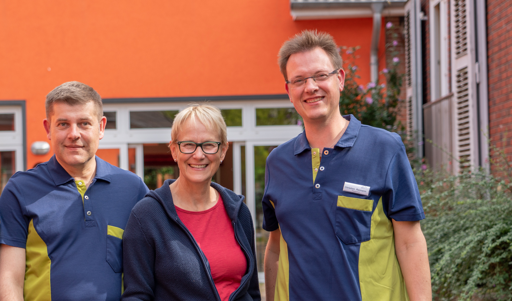 Zwei Männer und eine Frau in Dienstkleidung schauen lachend in die Kamera. Die Frau steht in der Mitte.